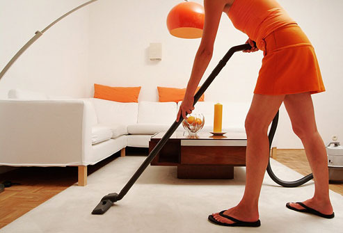 A person in orange is using a vacuum on a gray carpet.