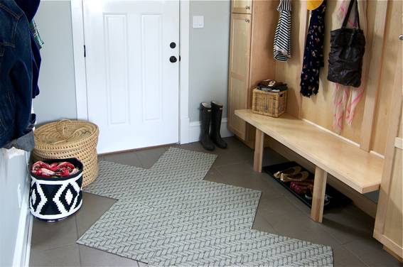 Squares of rug run down the center of the mud room with a cabinet and bench setup on the right