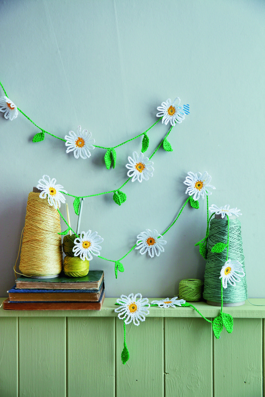 A wall decorated with Crochet Daisy Garland, few books and wool bundles.