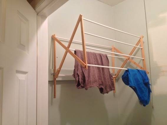 A drying rack mounted in a closet, with clothing drying on it.
