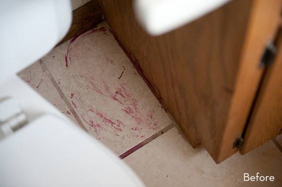 Something red stains the floor near a wood door in a bathroom.