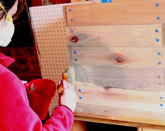 Woman is painting to a wooden deck with brush.