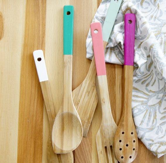 Light wooden spoons with colorful handles are on a woodsn surface.