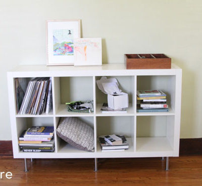 Long white bookshelf with a few books and pillows inside the shelves.