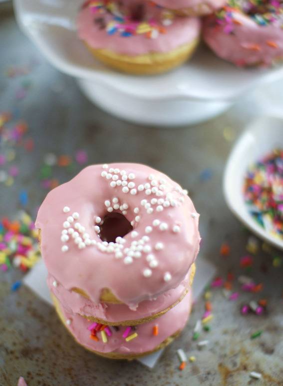 Pink donuts are stacked near a white container.