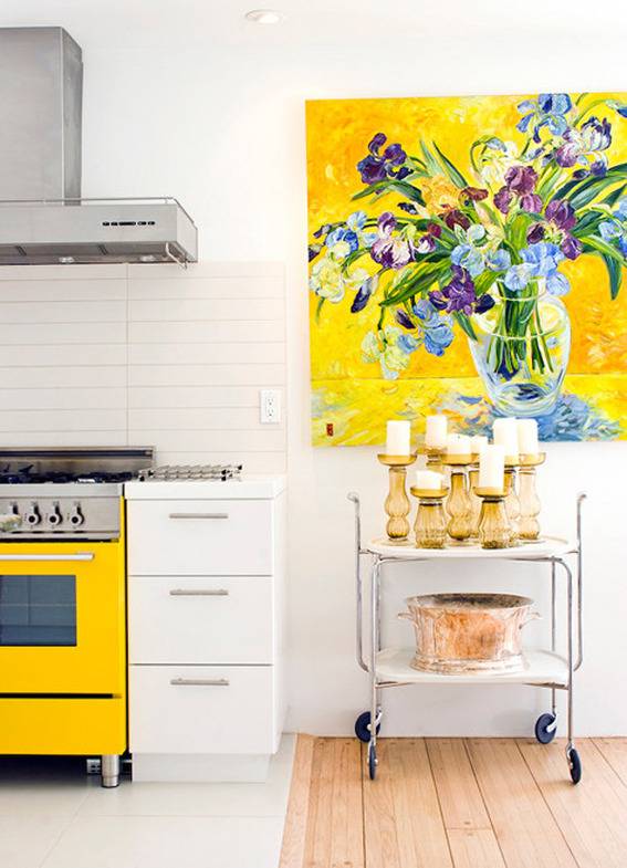 A white kitchen has a yellow oven, candles and picture on the wall.