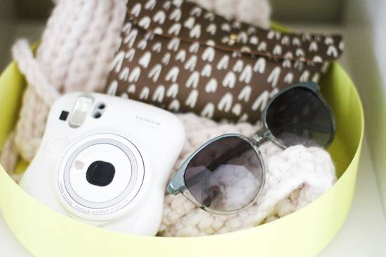 A bowl with a camera, sunglasses, a scarf, and wallet.