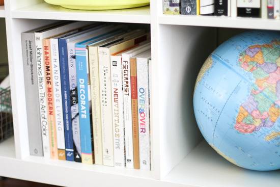 A globe and books are kept in a white bookshelf.