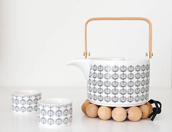 A pattern design tea kettle is next to two pattern design tea mugs.