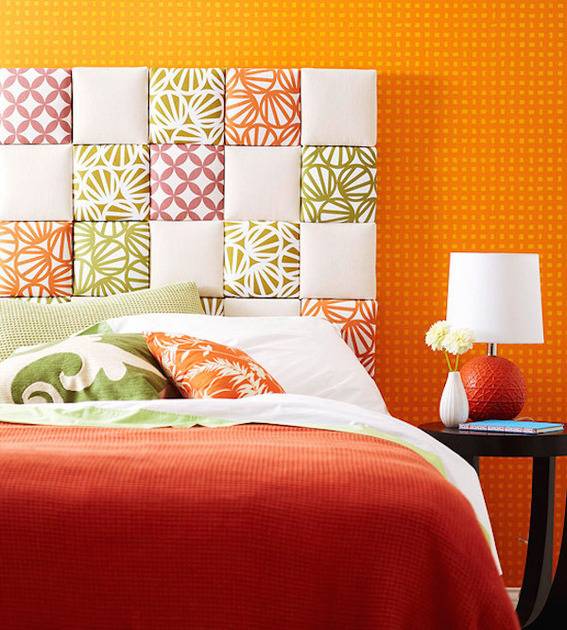 Red, green, orange, and white patchwork tile creates a headboard for a bed against an orange wall.