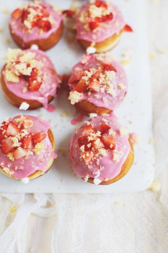 Donuts with pink icing, and strawberries on top.