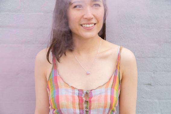 A woman with shoulder length brown hair, wearing a multicolored striped tank top with buttons in the front is smiling at something.