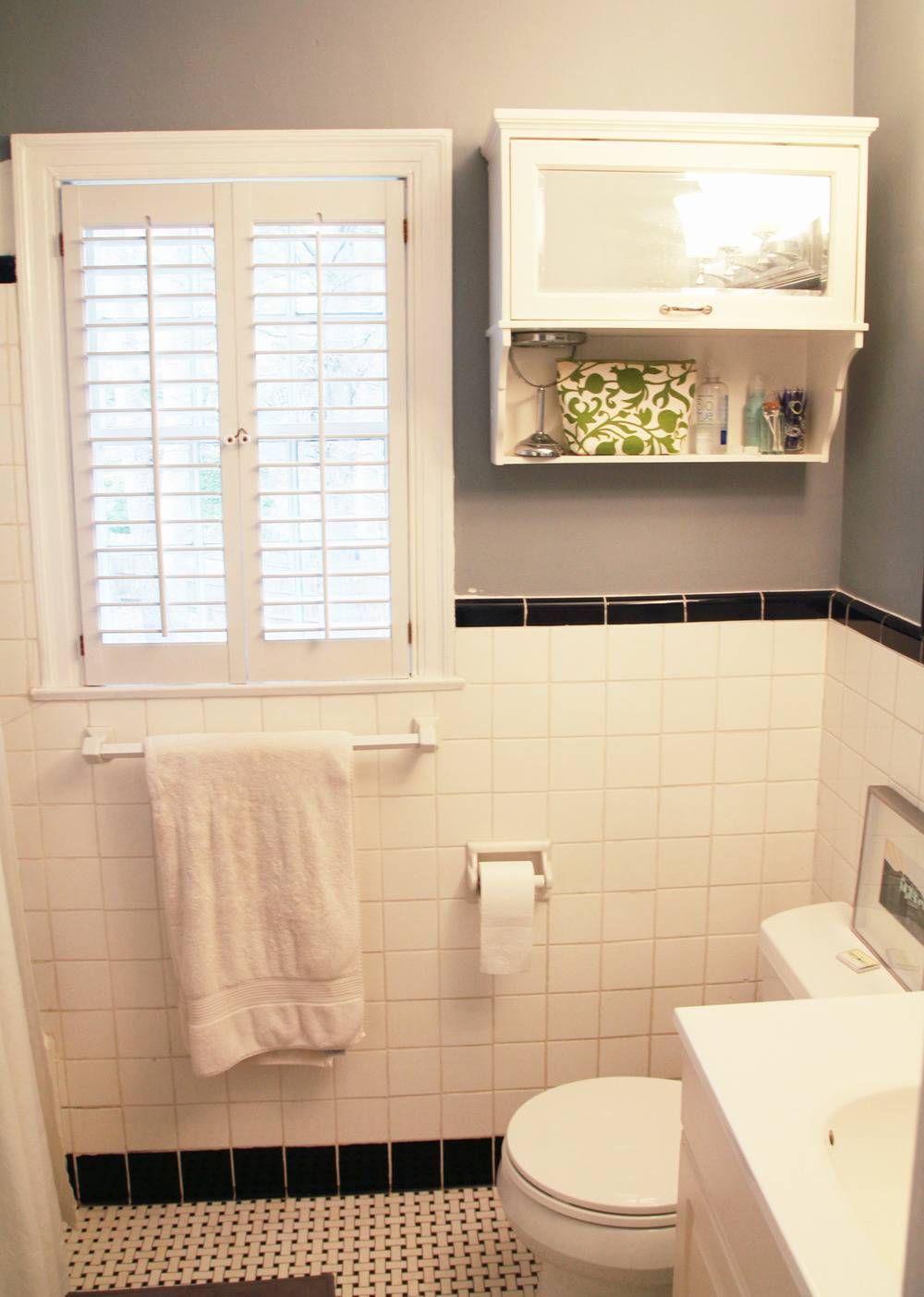 Light shines through a slatted shuttered window in a bathroom with gray walls.