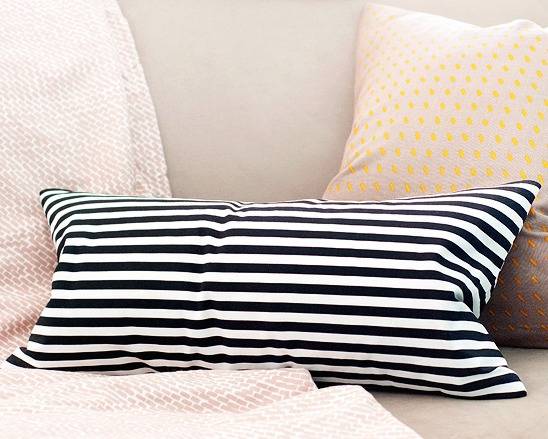 A bed has a black and white striped pillow on it.