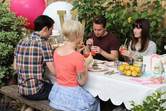 Two couples are eating at a picnic table with pink and white balloons.