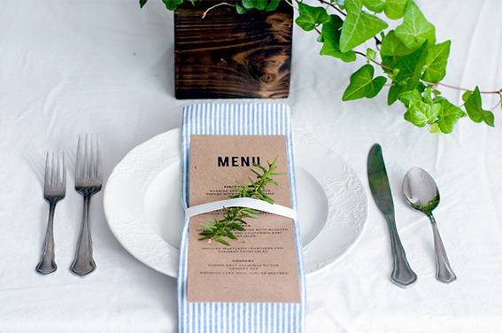 "Dinning in white surface with wrapped menu card on plate and spoons and knife."