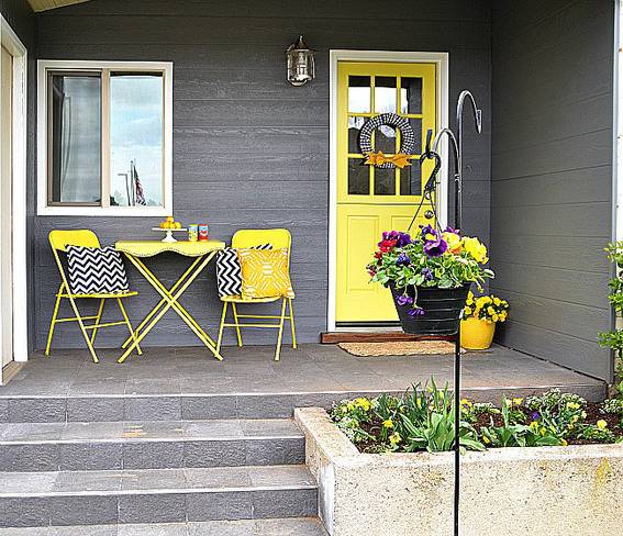 A grey house with yelow door and porch furnishings.