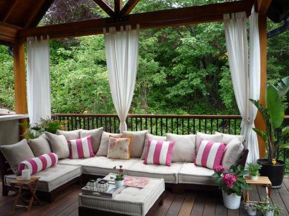 "Wooden corridor with sofa,cushions plants, trees and outdoor curtain."