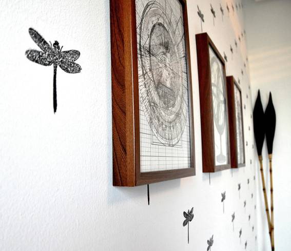 A dragonfly and other artwork hangs on a white wall.
