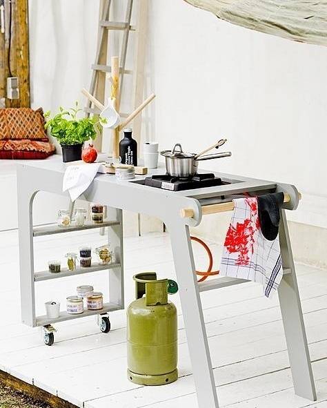 A pot sits on the eye of a propane stove set up on a bright white porch.