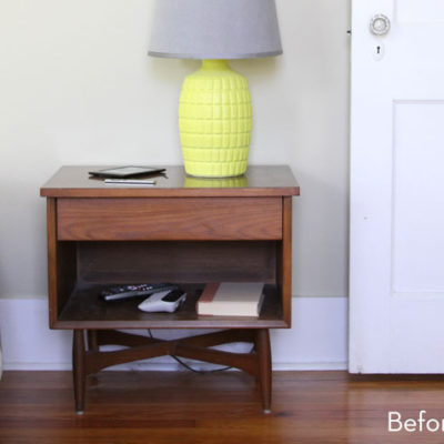 Wooden nightstand with a yellow lamp, book, and controllers.