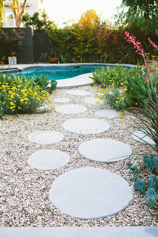 A backyard with a round step path set in gravel leading the way to an inground pool.