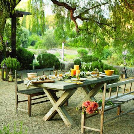 A traditional picnic table with separate bench seats and bright candles sits in a green garden.