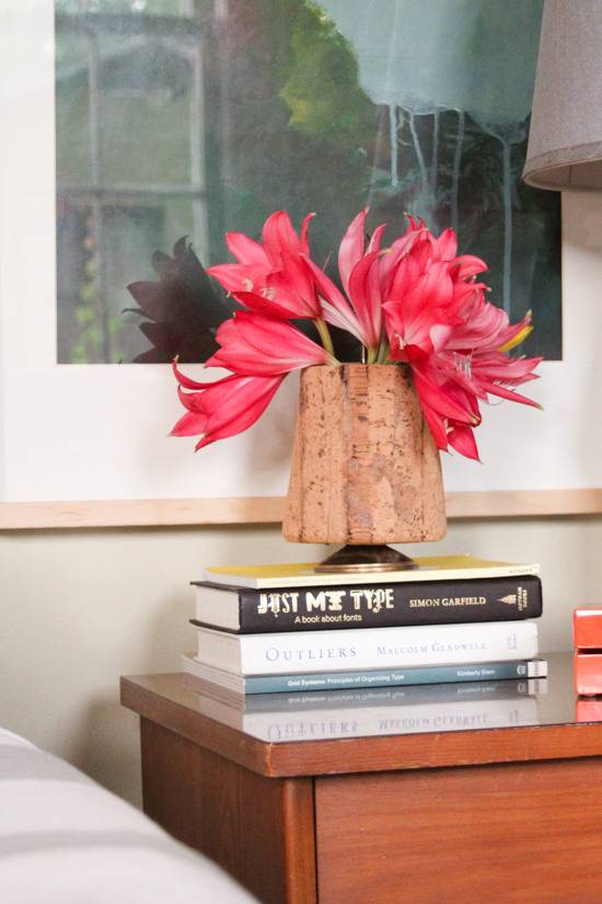 A hot orange plant sits on books in front of a picture.