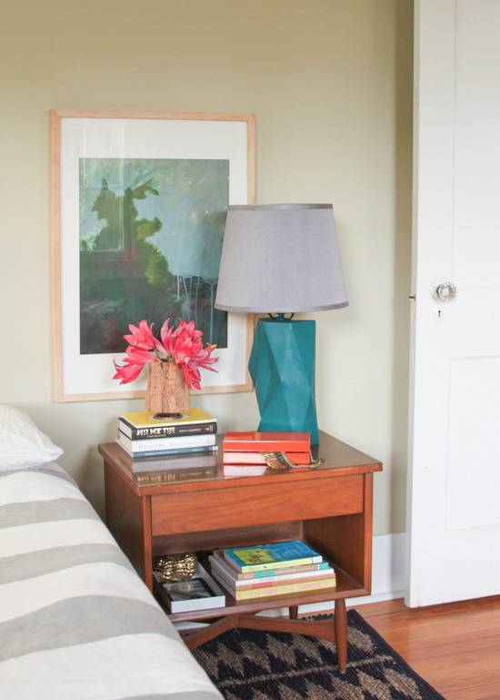 "Bedroom with nightstand,wall hanging and some books on the table."