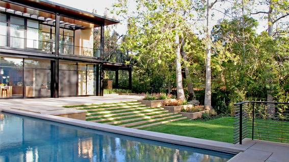 The backside exterior of a modern two story house with a pool and grass covered steps leading down to the lawn.