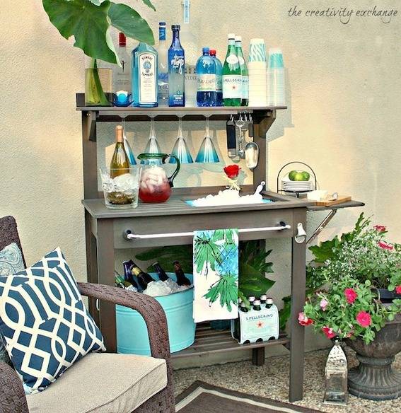 Patio with an armchair and planter next to a gray bar cart holding many bottles.