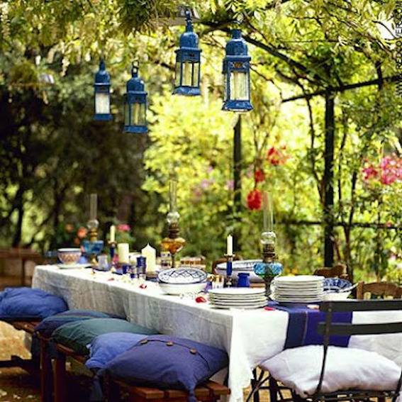 Blue and white pillows sit on stools set up at a table prepared for a garden party.
