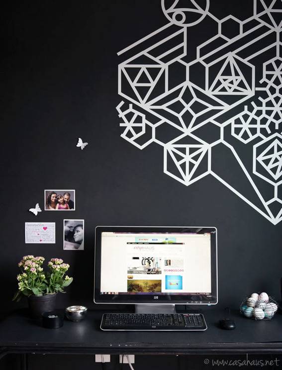 A black wall with som ewhite designs, a computer on a desk in between a bowl of golf balls and a white plant.