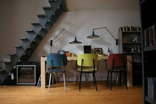 A contemporary room has colorful chairs and loft steps.