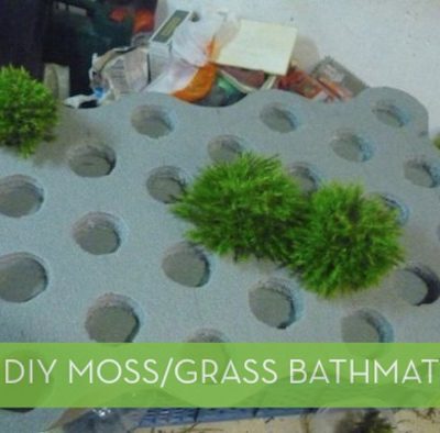 A white DIY moss bathmat has small patches of grass on it.
