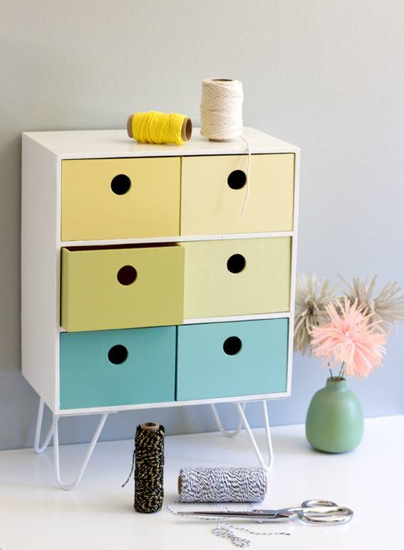 A white mid-century modern dresser has drawers painted yellow green and blue.