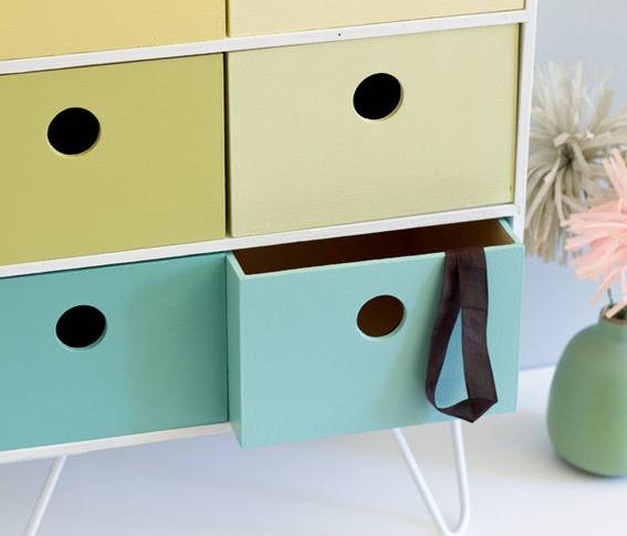 Green and blue drawers with holes for handles, one blue drawer is open with a black ribbon hanging out.