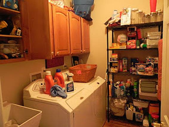 A cluttered laundry room has a large, stocked shelf.