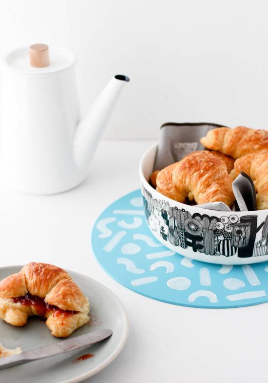A croissant cut in half with jam in it sits on a plate near a black and white patterned bowl full of croissants.