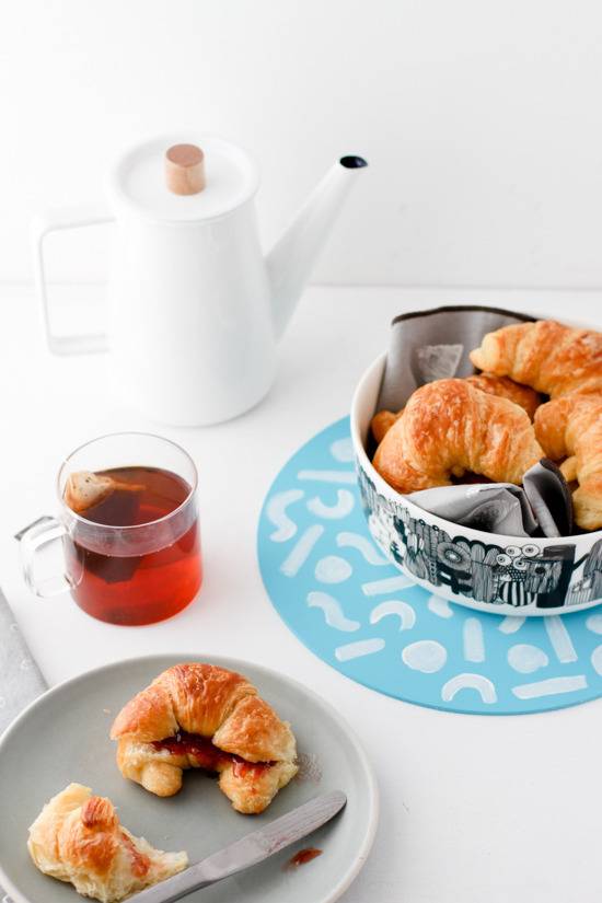 A white table with croissants, and tea in a white kettle.