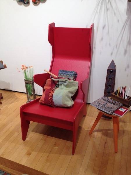 Red chair has a large multicolored bag on top of it.