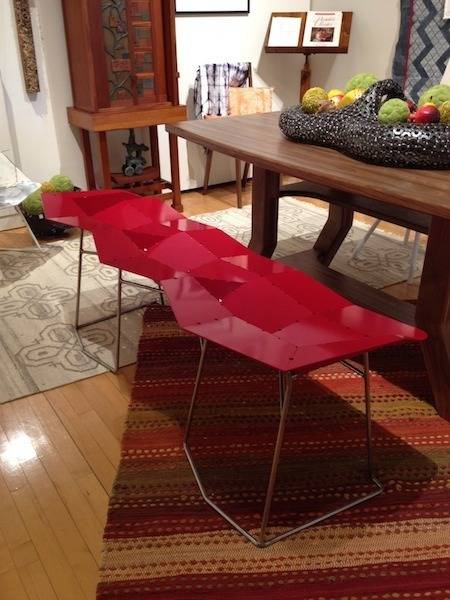A wooden table with a red shiny angular bench on one side.