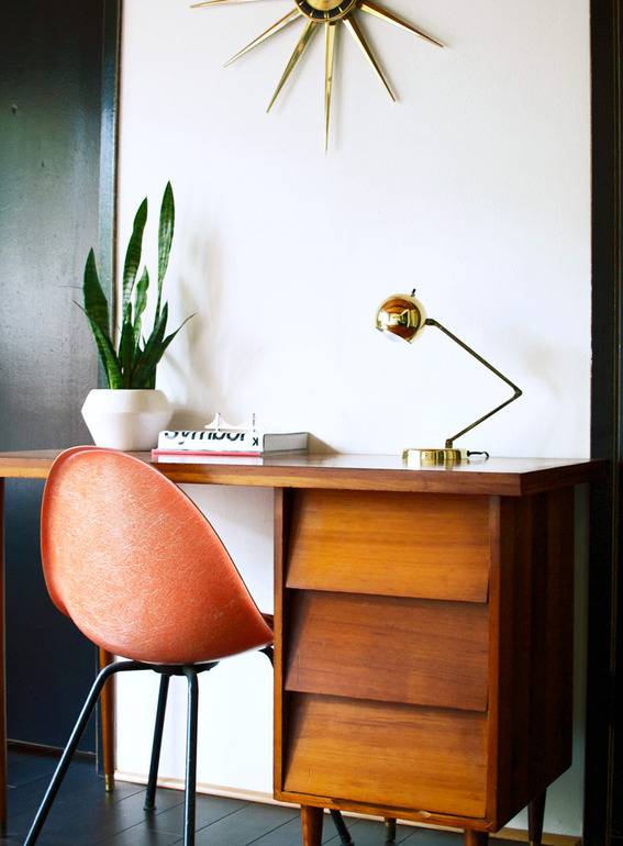 A plastic orange 50's style chair sits at an antique wood desk.