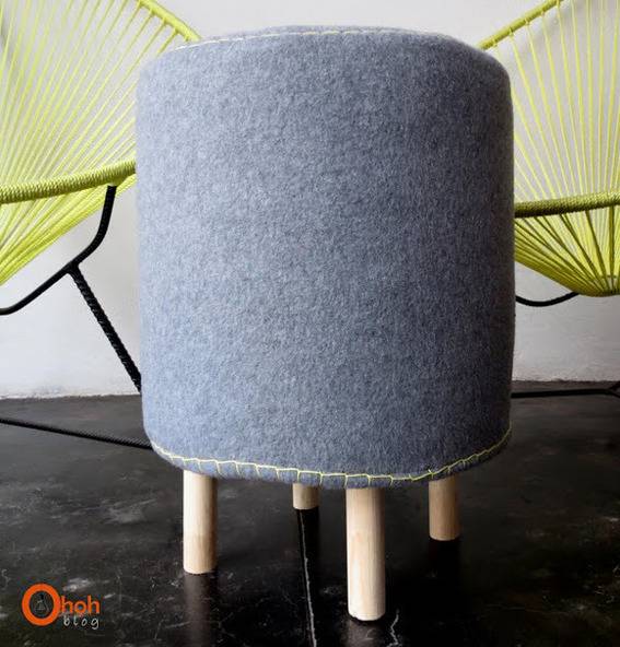 Tall grey, round seat, with small wooden peg legs; in front of two green yarn chairs.
