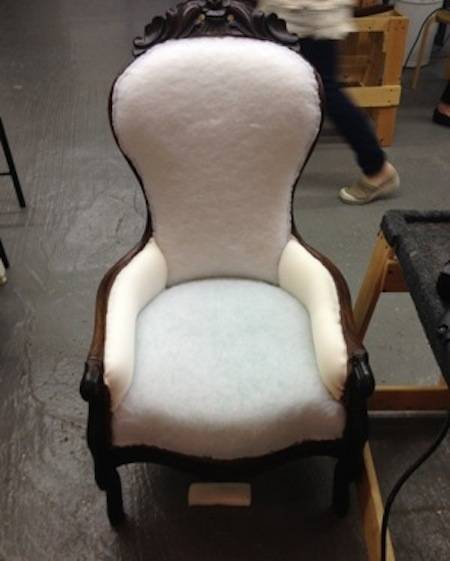 A white chair with brown legs on a grey floor.