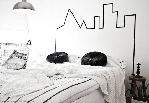 A bed has two round black pillows and a city design on the wall behind it.