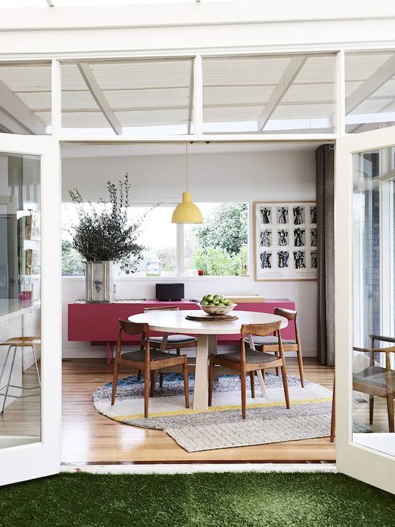 A white room has red accent furniture and a green turf rug.