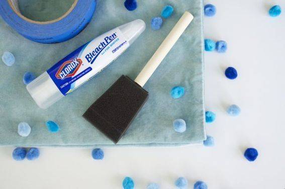 A bleach pen and blue tape is next to a sponge brush