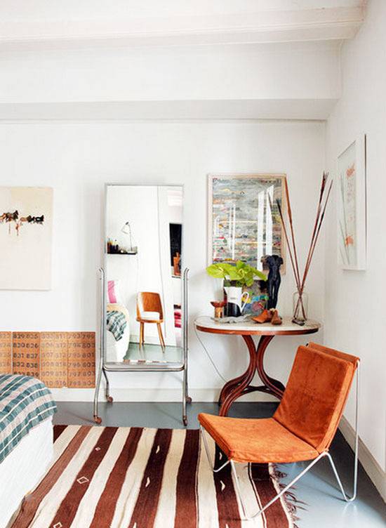 Bedroom having a bed, orange chair and a mirror.