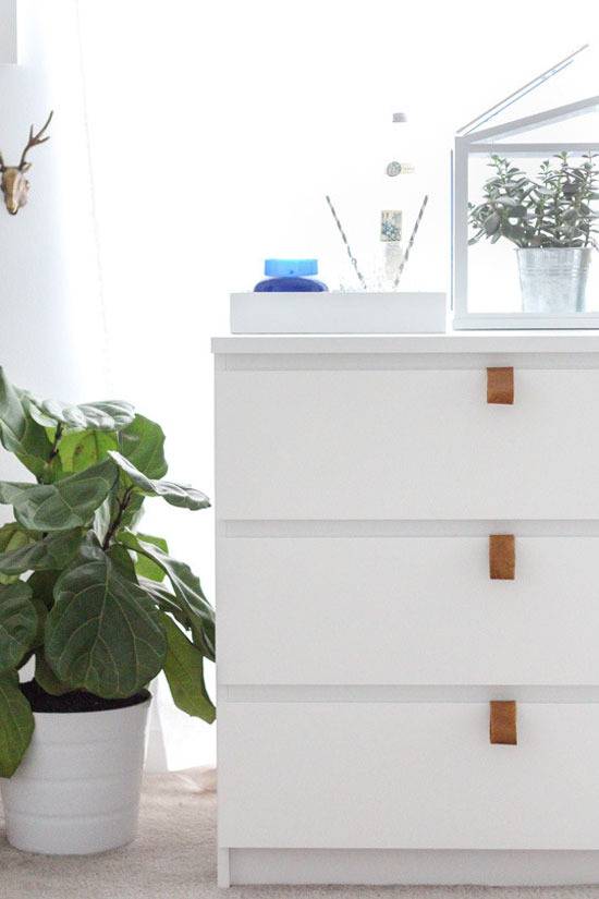 A three drawer cabinet with a potted plant next to it and a blue jar on top of it.